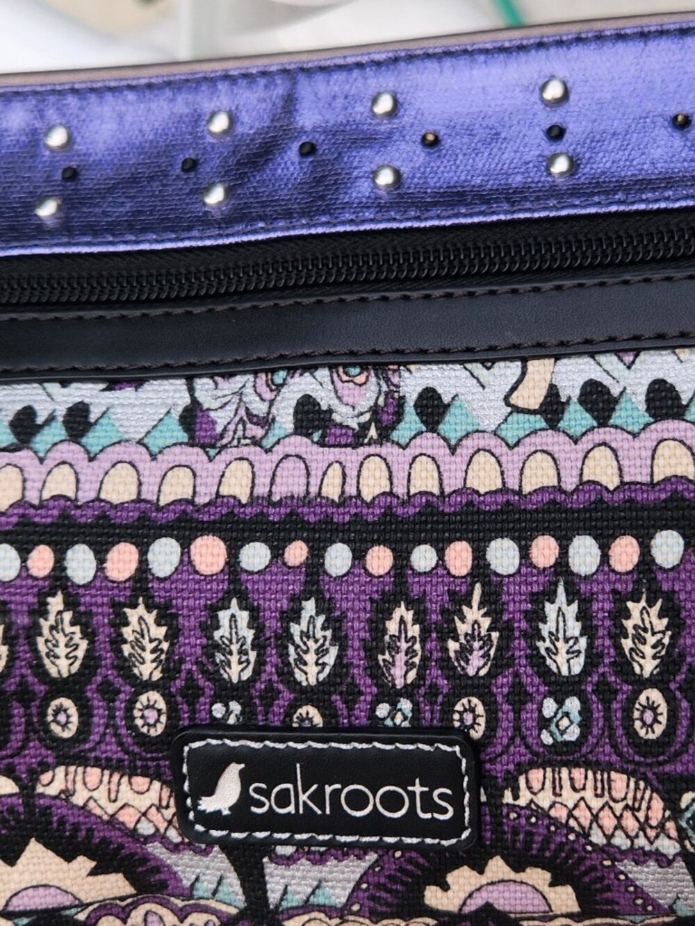 SAKROOTS Crossbody bag with 2 straps; purple metallic panel on top.